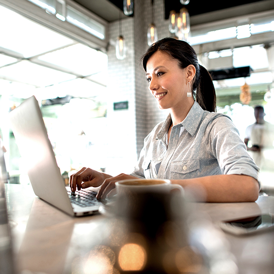 mujer escribiendo en un portatil mientras esta en una cafeteria